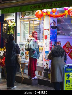 Una donna dell'Asia orientale che aspetta un chiosco nella città cinese, soho, Londra. Foto Stock