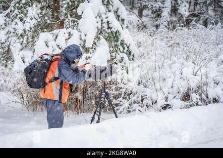 Cameraman professionista con fotocamera per riprese naturali nella foresta di neve. Concetto dietro la scena Foto Stock