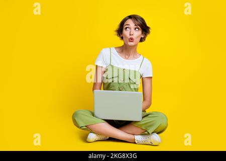 Foto a grandezza naturale di carino giovane donna lavoro netbook aspetto impressionato spazio vuoto indossare abiti cachi alla moda isolato su sfondo di colore giallo Foto Stock