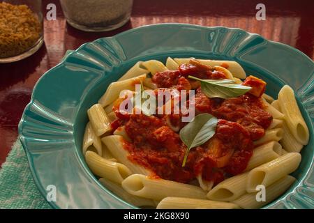 Goiânia, Goias, Brasile – 22 novembre 2022: Un piatto verde brillante con una porzione di pasta (penne) con salsa di pomodoro e foglie di basilico. Foto Stock