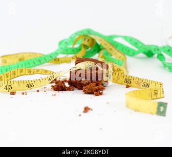 pezzo di torta al cioccolato avvolto con una dieta gialla a nastro di misurazione e immagine di concetto di vita sana. Foto Stock