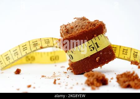pezzo di torta al cioccolato avvolto con una dieta gialla a nastro di misurazione e immagine di concetto di vita sana. Foto Stock
