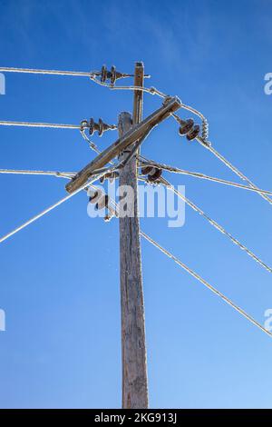 Un palo in legno e le linee elettriche coperte di brina di bue in una chiara giornata invernale Foto Stock