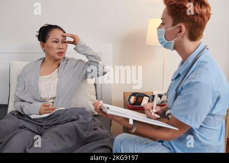 Donna anziana lamentarsi di mal di testa al medico che la visita a casa Foto Stock