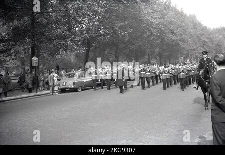 1950s, storico, un poliziotto a cavallo di fronte a una band che gioca mentre camminano lungo una strada, forse l'Esercito della salvezza, che conduce una marcia di ex-servicemen e membri sindacali, Parliament Hill, Westminster, Londra, Inghilterra, REGNO UNITO. Foto Stock