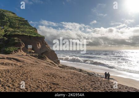 Una coppia si trova sulla spiaggia da spettacolari scogliere illuminate dal sole a West Bay, Dorset, Regno Unito Foto Stock