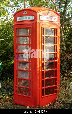 Cassetta telefonica rossa vintage convertita in un defibrillatore situato nel villaggio Dorset di Witchampton, vicino a Wimborne, Dorset, Regno Unito. Foto Stock