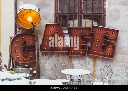 Accogliente caffetteria, arrugginito cartello con lampade e riflettori vintage nel centro storico di riga, in Lettonia, in inverno con tavoli e sedie coperti di neve Foto Stock