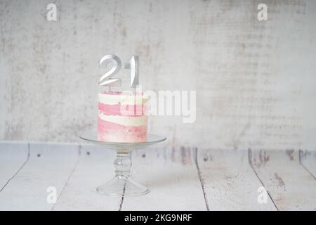 21st torta di compleanno torta rosa e argento con alcuni spruzzi e 21st candela su uno sfondo di legno bianco. Foto Stock