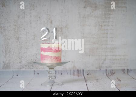 21st torta di compleanno torta rosa e argento con alcuni spruzzi e 21st candela su uno sfondo di legno bianco. Foto Stock