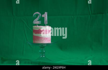 21st torta di compleanno torta rosa e argento con alcuni spruzzi e 21st candela su sfondo verde. Foto Stock