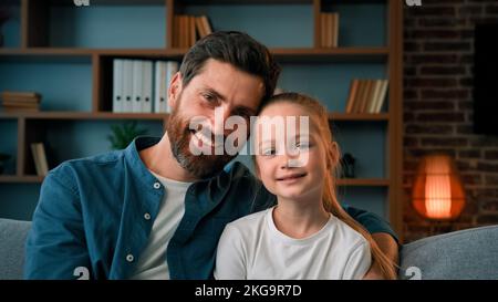 Felice famiglia caucasica persone di generazione diversa bella figlia e padre si siedono sul divano posando insieme a casa papà abbracciare amata bambina Foto Stock