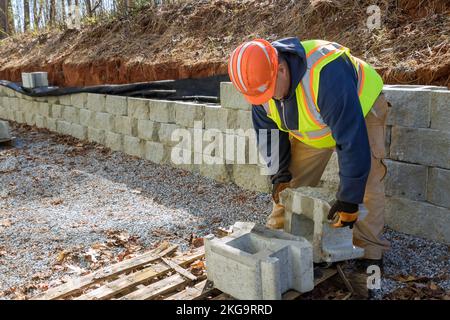 Durante la costruzione di un nuovo progetto di parete di ritegno, c'era un appaltatore che installava una parete in blocchi di cemento Foto Stock