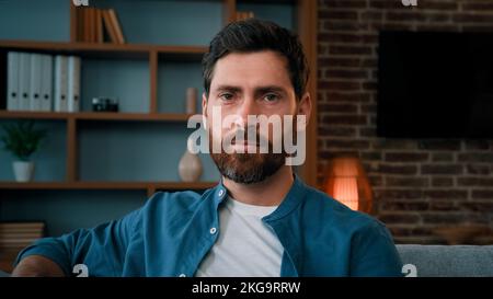 Testa sparato bello barbuto tipo caucasico sicuro serio 30s ritratto maschio indossa casual camicia blu attraente uomo caucasico proprietario di casa cliente sedersi sopra Foto Stock