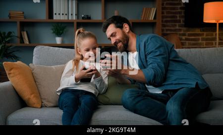 L'uomo caucasico e la bambina del capretto si siedono insieme nel paese tengono il telefono moderno che naviga il soddisfare di mezzi gioca i giochi in linea adulto dad insegnano l'uso della figlia del bambino Foto Stock