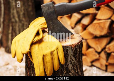 ascia incastrata in un ponte di legno e guanti protettivi in pelle gialla Foto Stock