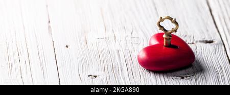 Piccolo cuore rosso intagliato a mano con chiave d'oro sul tavolo rustico di legno - la chiave al vostro concetto di cuore Foto Stock