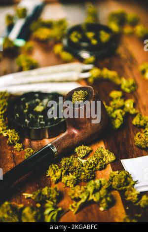 Droghe di marijuana su un tavolo di legno. Pipa fumante, macinacaffè e cbd sativa o indica tgk boccioli. Carta per giunti Foto Stock