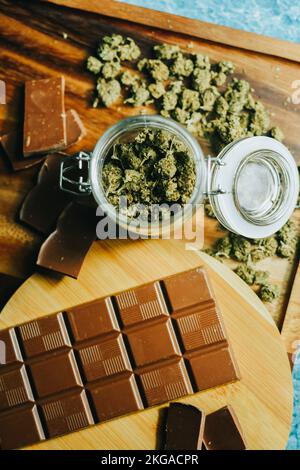 Cioccolato con marijuana sullo sfondo di un tavolo di legno e coni di marijuana. CBD e THC, sativa e indica. erba marijuana nel cibo Foto Stock