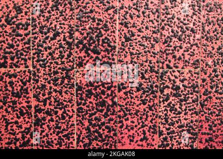 Superficie ruvida con sfondo rosso e macchie nere che fanno parte della decorazione di una parete esterna in un edificio Foto Stock