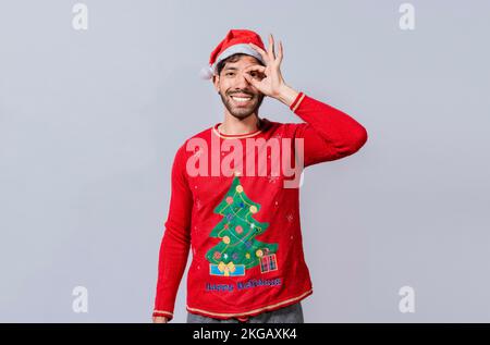 Divertente giovane uomo in cappello di natale guardando attraverso le dita. Divertente ragazzo di natale facendo gesto e guardando attraverso le dita, l'uomo nel cappello di natale fare Foto Stock