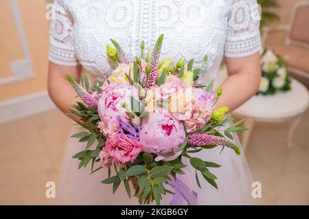 Bouquet nuziale bello di fiori rosa matrimonio in mano della sposa. Primo piano di uno studio interno con sfondo luminoso. Bouquet con peonie Foto Stock
