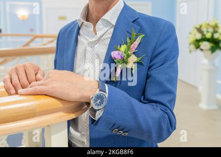 Uomo elegante in un suit.boutonniere di eremurus, eustoma bianco e verde attaccato alla giacca blu grooms. Dettagli e caratteristiche del matrimonio Foto Stock