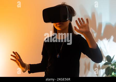 Le ragazze adolescenti si divertono a giocare a metaverse di realtà virtuale con gli occhiali VR, giocare a videogame, guardare film, ascoltare musica, fare shopping. Neon colorato Foto Stock