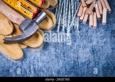 Guanti di protezione in pelle martellata pila di chiodi metallici e tasselli su fondo metallico graffiato concetto di costruzione. Foto Stock