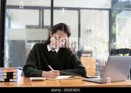 studiare a distanza da casa, utilizzare un computer portatile, prendere appunti sul blocco note durante la lezione online, e-learning concetto, sorridendo Foto Stock