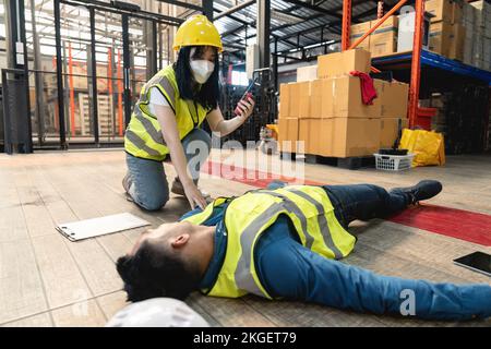 Una lavoratrice di magazzino che utilizza un walkie-talkie ha chiamato la squadra di pronto soccorso della fabbrica per salvare un uomo inconscio. passaggio o blackout, non sicuro Foto Stock