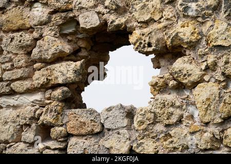 Vecchio muro di pietra di un castello con vista sul cielo. Muro difensivo con scappatoia. Foto Stock