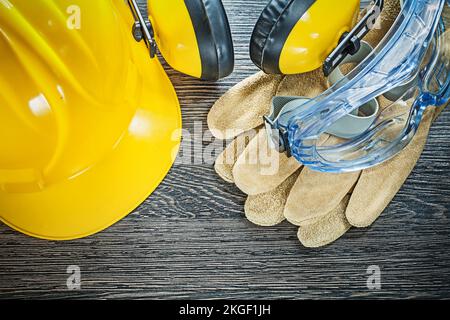 Cappuccio di sicurezza guanti in pelle occhiali cuffie su tavola di legno. Foto Stock