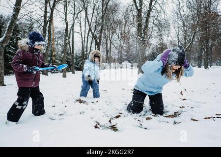 Famiglia felice, amici, madre e bambini divertirsi all'aperto in inverno neve sfondo natura. Mamma e due ragazzi giocano a snowball nel parco invernale all'aperto Foto Stock
