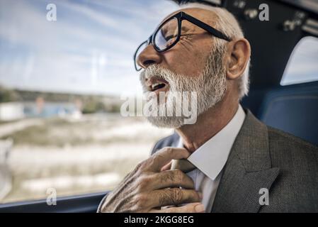 Primo piano di un professionista anziano di sesso maschile che si sente a disagio mentre si siede in treno. Il pendolari senior sta facendo la faccia avendo un serio sondaggio sulla salute Foto Stock