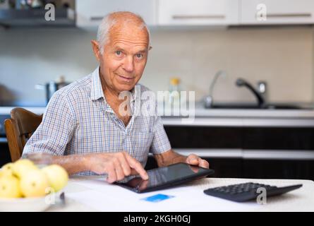 Nonno che effettua il pagamento online da tablet digitale. Anziano anziano nonno caucasico che paga le fatture in linea Foto Stock