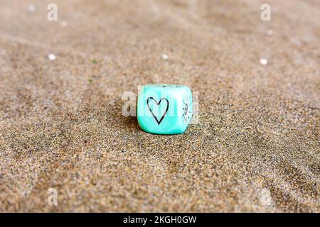 Simboli del tempo del sole e del cuore sui lati del cubo di plastica blu. Dadi divertenti da gioco sulla sabbia. Concetto di San Valentino. Simbolo dell'amore. Immagine ravvicinata con Foto Stock