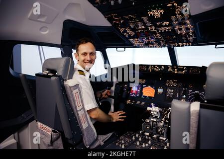 Pilota nel cockpit. Vista posteriore di un pilota maschio fiducioso che guarda sopra le spalle e sorride mentre si siede in cabina di pilotaggio Foto Stock