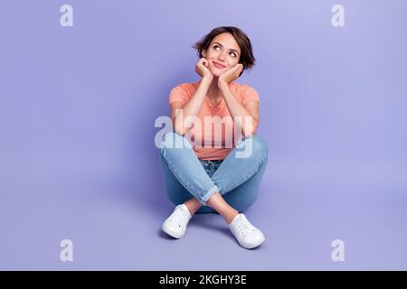 Full body foto di attraente giovane donna seduta pavimento guardare Dreamy spazio vuoto indossare abiti a righe trendy isolato su sfondo di colore viola Foto Stock