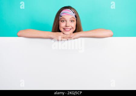 Foto di amara affascinante scolaretta sorridente tenendo grande cartellone bianco spazio vuoto isolato colore turchese sfondo Foto Stock