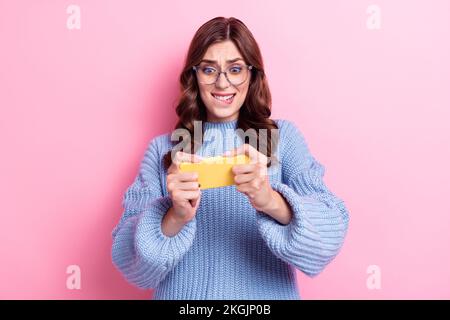 Ritratto di carino piuttosto preoccupato capelli ricci donna indossare occhiali blu maglia pullover nervoso telefono cellulare play web app isolato su sfondo rosa colore Foto Stock