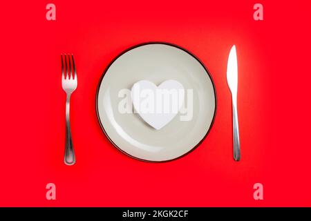 Concetto romantico di cena di giorno di valentines. Cuore sul piatto e argento su sfondo rosso. Foto Stock