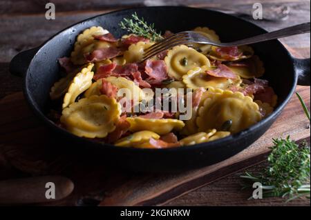 Ravioli con ripieno di funghi, prosciutto italiano, burro e semi di zucca. Servito in una teglia di ferro vecchio stile su un tavolo di legno. Foto Stock