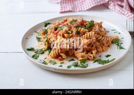 Pasta di tonno con salsa di pomodoro e parmigiano su un piatto bianco isolato su sfondo chiaro. Foto Stock