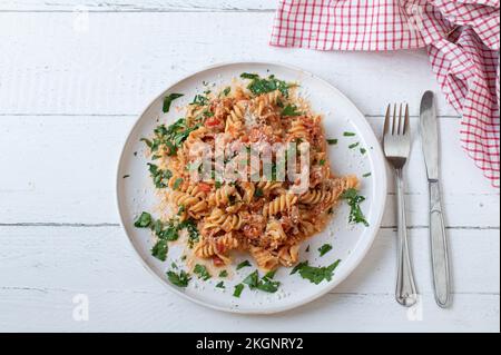 Pasta con salsa di pomodoro, tonno e parmigiano isolato su un piatto su fondo di legno bianco. Giacitura piatta Foto Stock