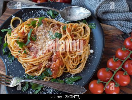 Spaghetti con salsa di pomodoro e parmigiano su un piatto scuro. Cucinato in casa su sfondo rustico Foto Stock