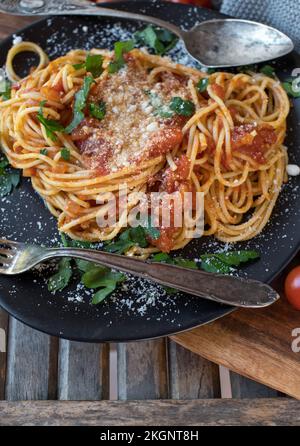 Spaghetti tradizionali con salsa di pomodoro e parmigiano su un piatto scuro su fondo di legno Foto Stock