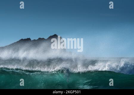 Spray soffiato dalla cresta di un'onda che si rompe a Fistral Bay con Goose Rock sullo sfondo a Newquay in Cornovaglia in Inghilterra nel Regno Unito. Foto Stock