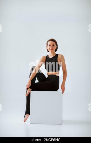 Donna matura sorridente in abbigliamento sportivo nero su sfondo bianco Foto Stock
