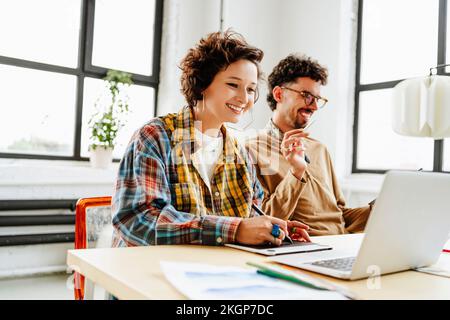 Buon designer grafico con un collega che utilizza un computer portatile alla scrivania in ufficio Foto Stock